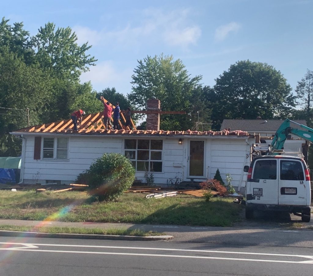 A crew of guys removing the roof and framing for the roof from a small, 1-story roof